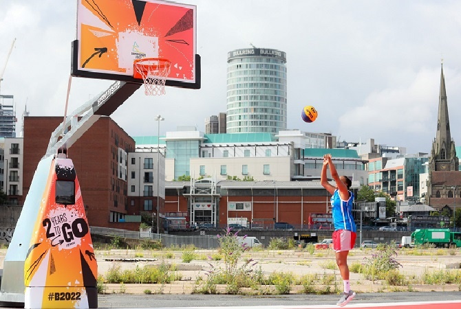 Athlete throwing basketball towards hoop on stand with "2 years to go" advertising on a concrete car park