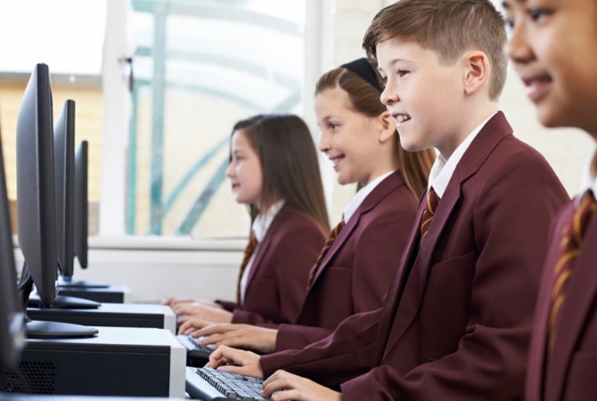 Children in school uniform sitting in a classroom in front of computers
