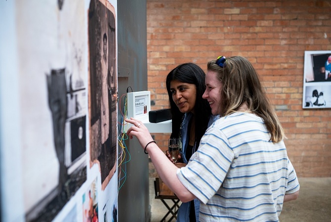 Two women look and touch a piece of art at an exhibition