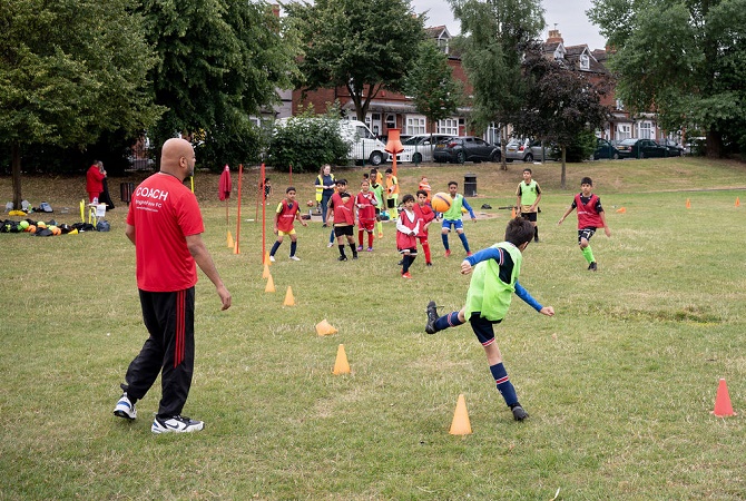 A football coach overseeing a football coaching session with a group of children kicking a football