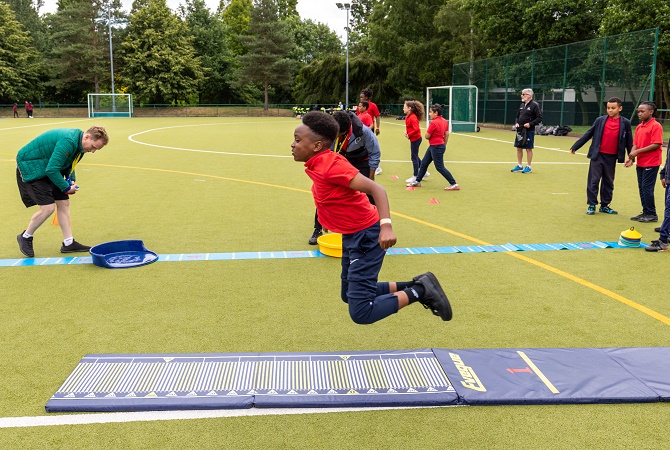 Young boy in a red t-shirt participates in a long jump activity at a Bring the Power event