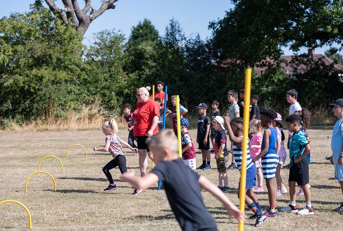 A group of children taking part in an obstacle race with a coach supervising the activity