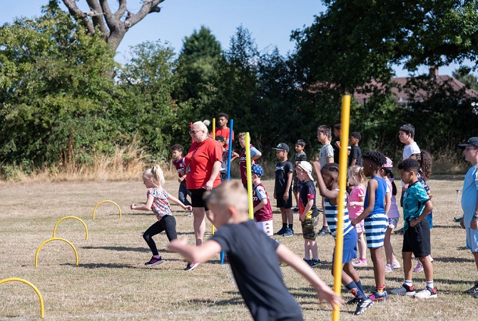 A group of children taking part in an obstacle race with a coach supervising the activity