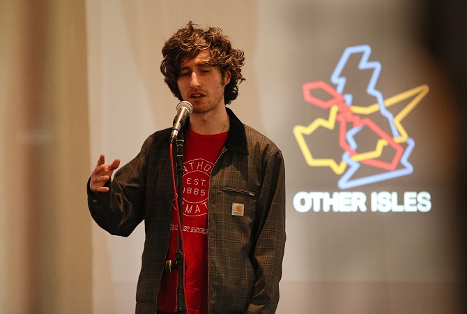 A man performs on stage in front of a microphone as part of the Other Isles live event