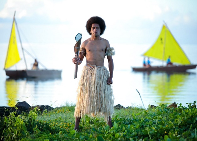 A local Fijian man in a traditional grass skirt holding the Baton